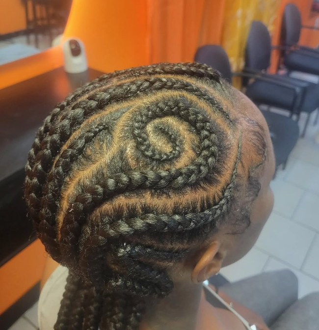 Braided updo with a floral bun, seen from the back in a salon setting, with “Hair By Adama” text overlaid Braided updo with a floral bun, seen from the back in a salon setting, with “Hair By Adama” text overlaid