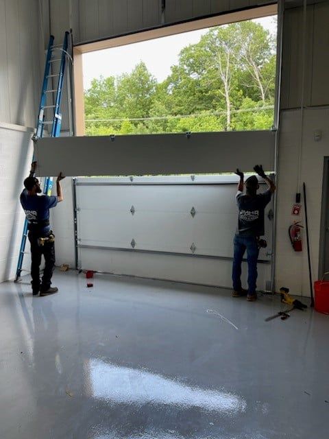 Two workers installing a large garage door in a bright workshop