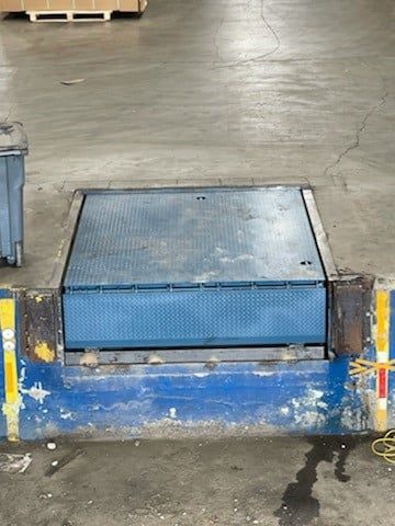 Blue industrial ramp or platform at a warehouse loading dock, set against a concrete floor.