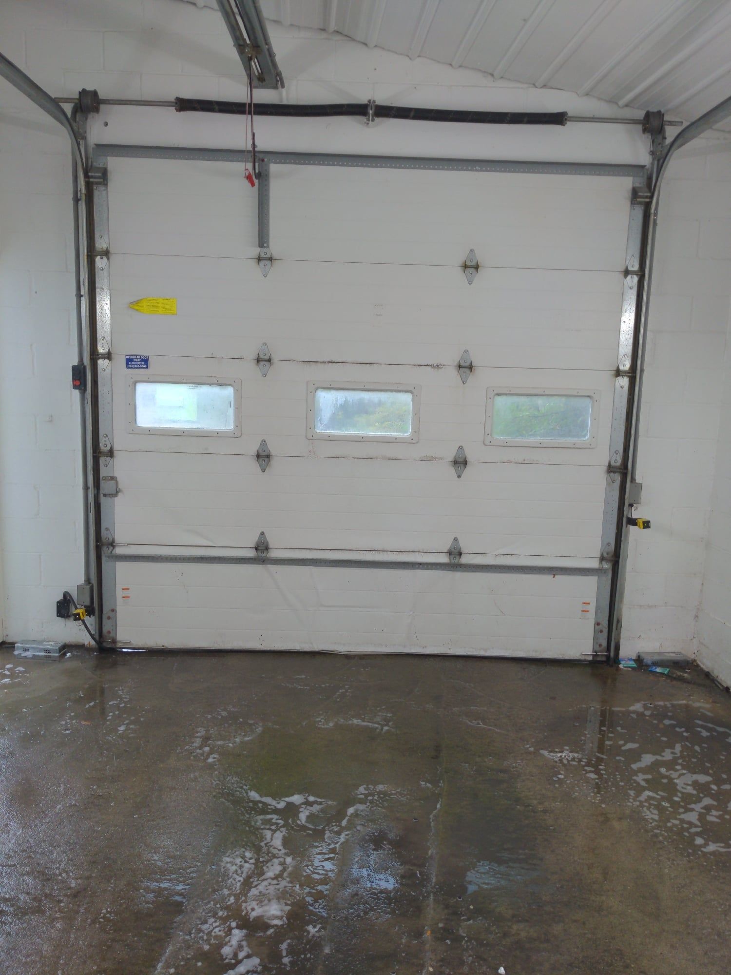Inside view of a garage with a white sectional overhead door and wet concrete floor.