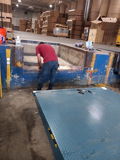 Worker in red shirt bending over a blue industrial loading dock in a warehouse.