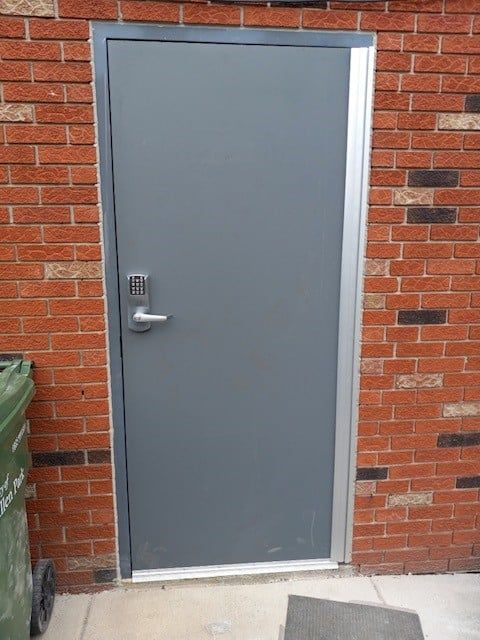 Gray metal door set in a red brick wall with a silver handle and frame.