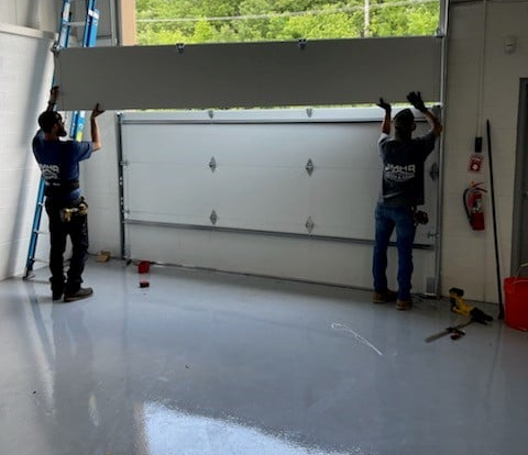 Two workers installing a large garage door in a bright workshop bay