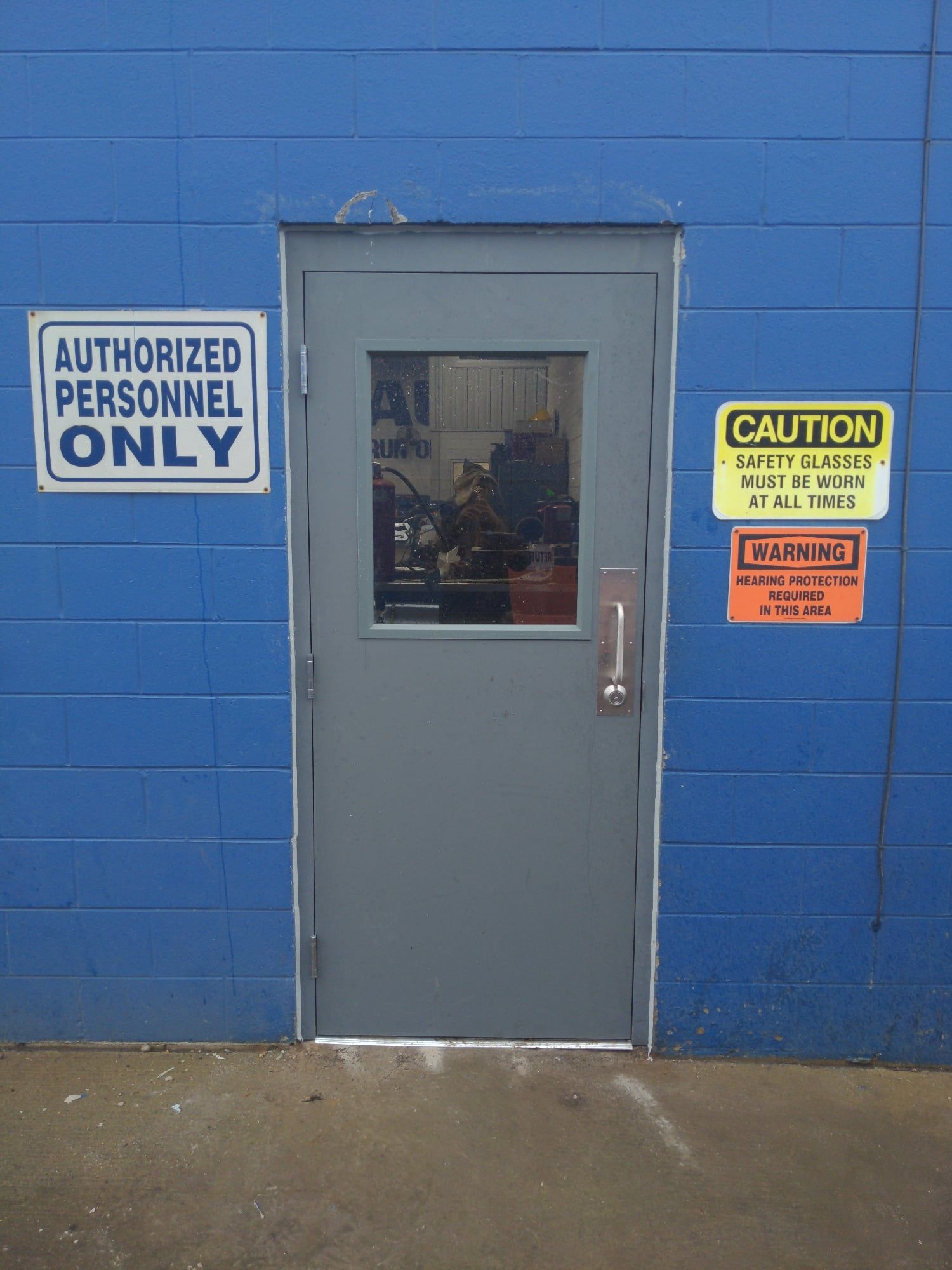 Blue wall with a gray door and warning signs, including “Authorized Personnel Only” and “Caution” notices.
