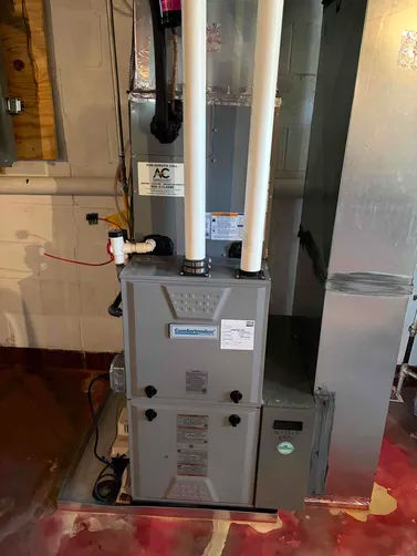 Furnace with two white PVC pipes, metal ductwork, and electrical components in a basement setting.