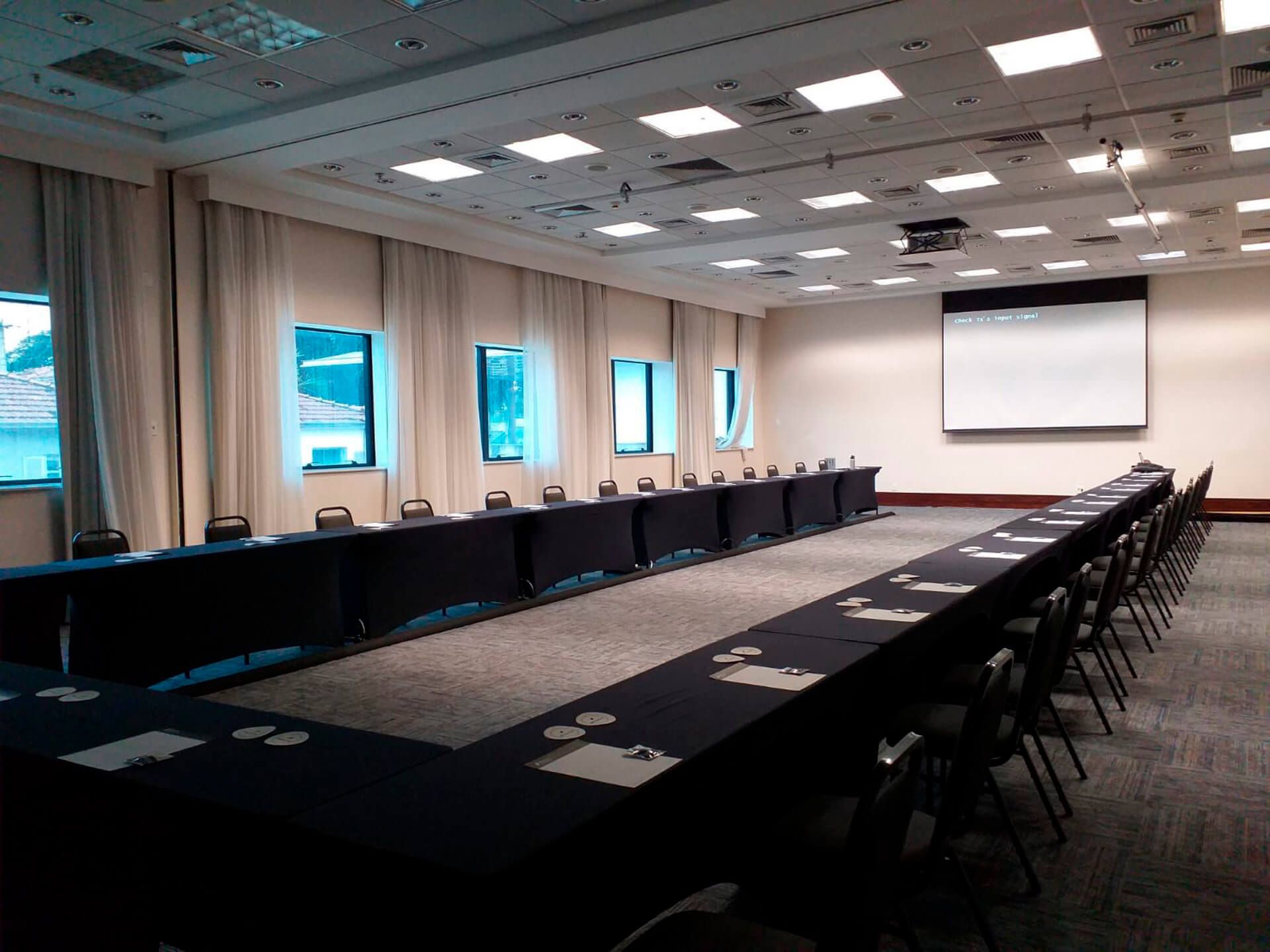 Uma grande sala de conferências com mesas e cadeiras e uma tela de projetor.