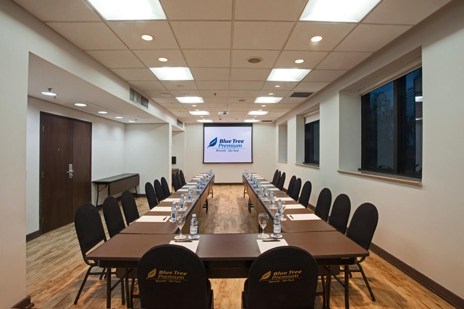 Uma grande sala de conferências com mesas e cadeiras e uma tela de projetor.