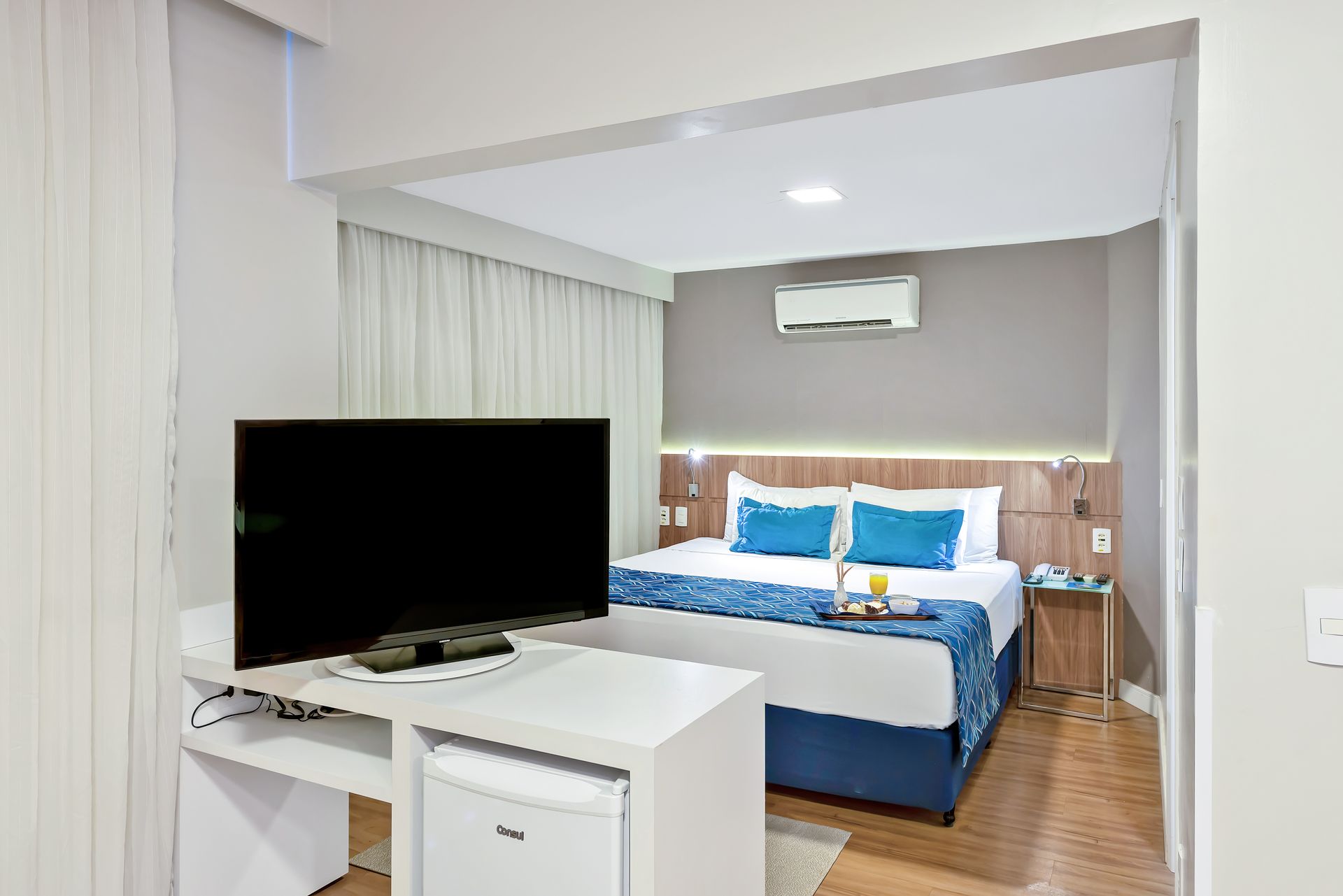 Um quarto de hotel com cama, escrivaninha, televisão e espelho.