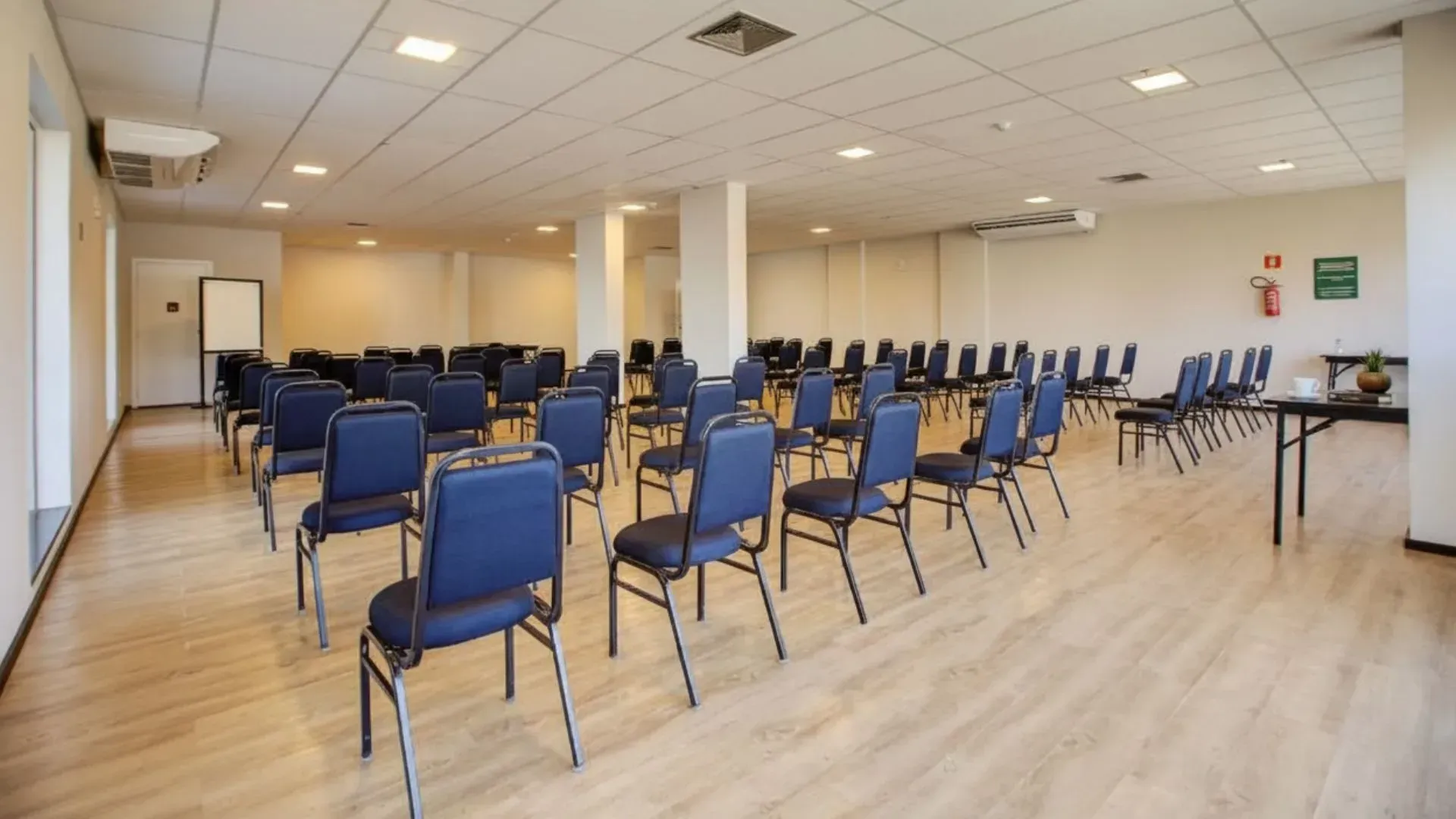 Uma sala grande com mesas e cadeiras e uma tela de projetor.