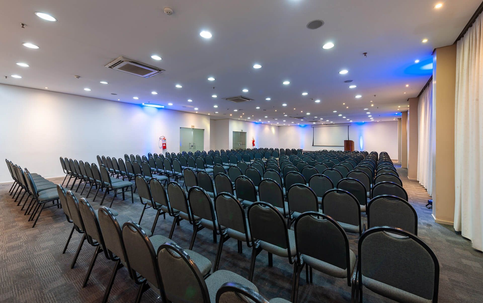 Uma grande sala de conferências com fileiras de cadeiras e um pódio.
