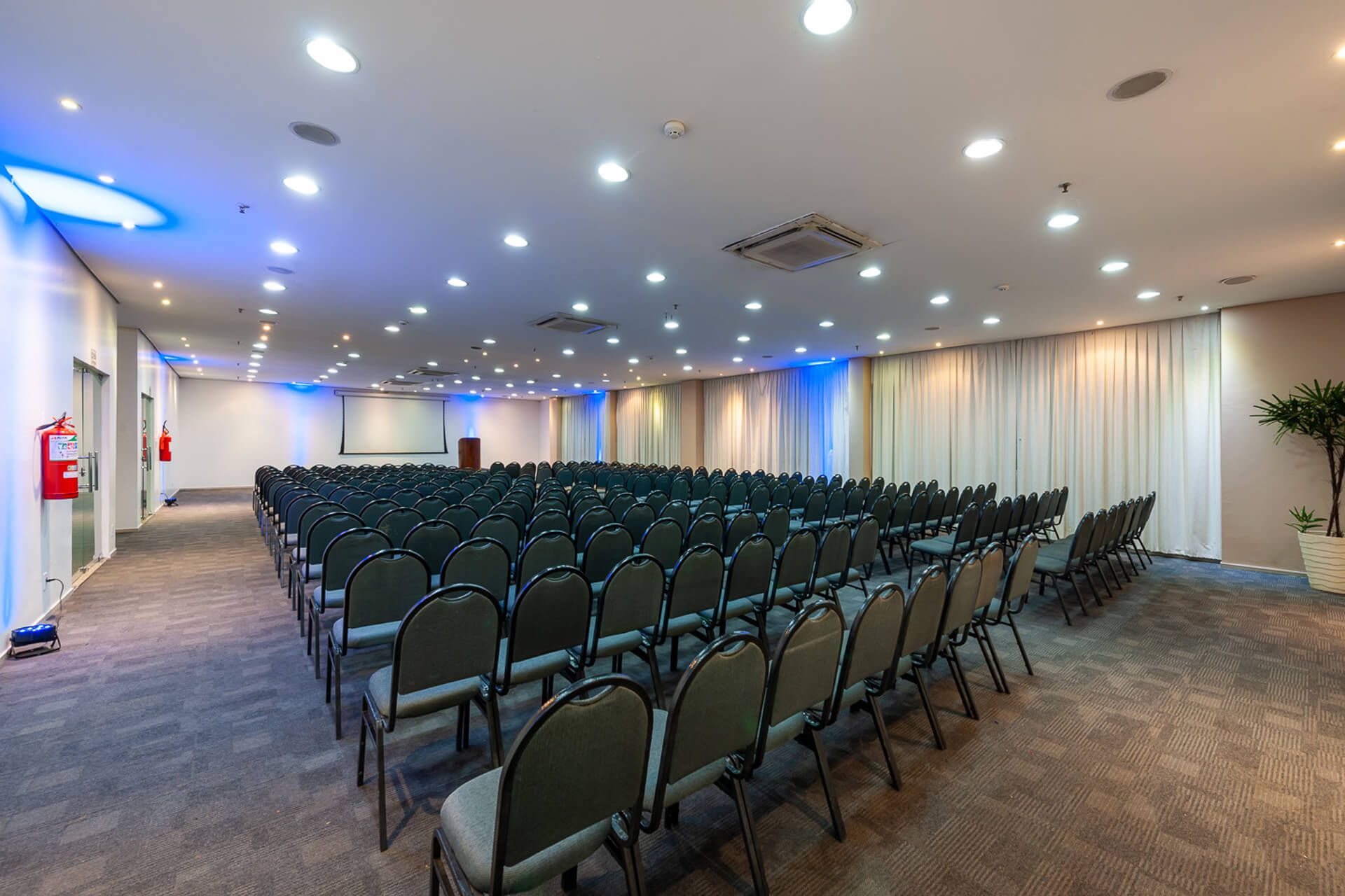 Uma grande sala de conferências com fileiras de cadeiras e uma tela de projetor.