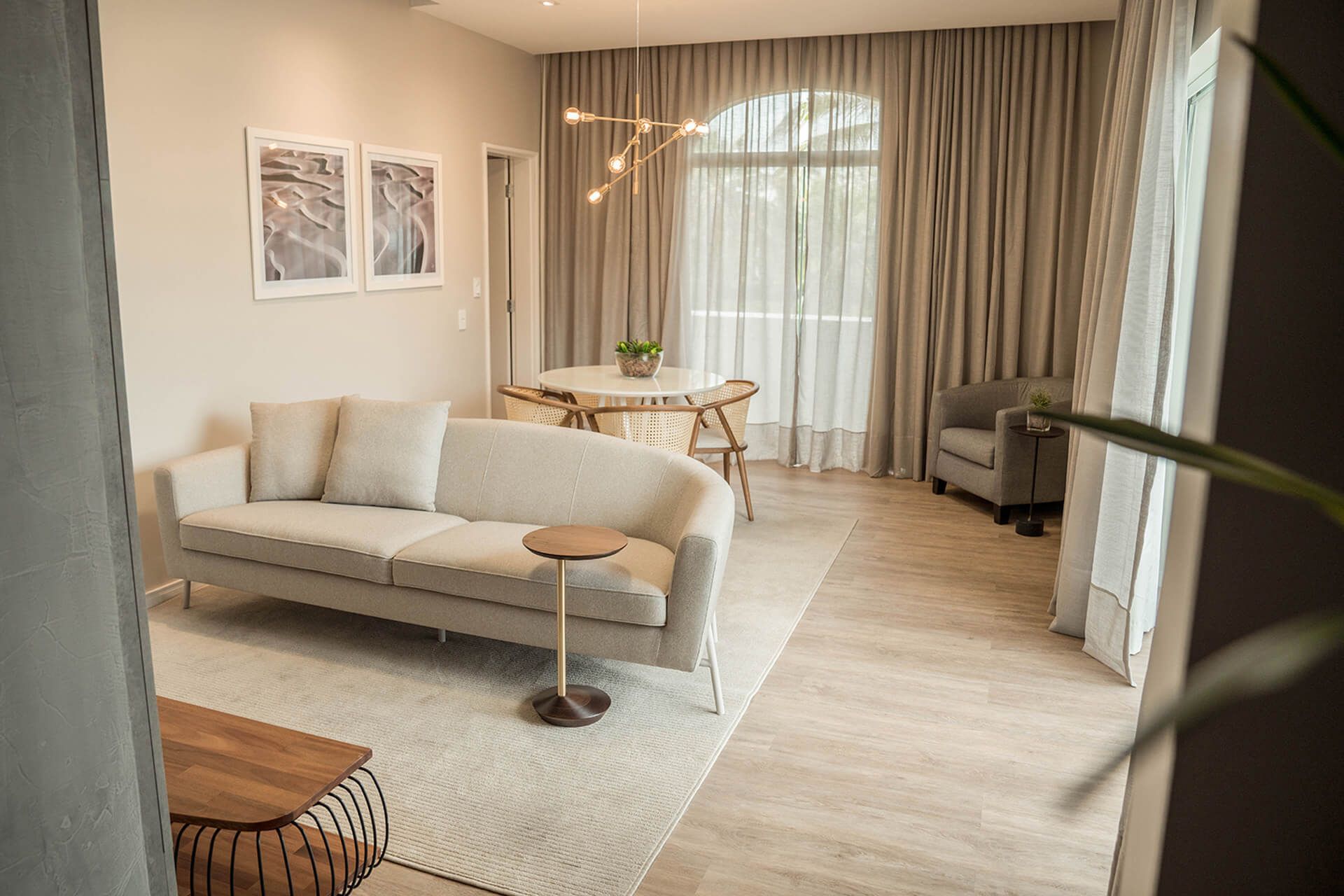 Uma sala de estar com sofá, mesa, cadeiras e cortinas.