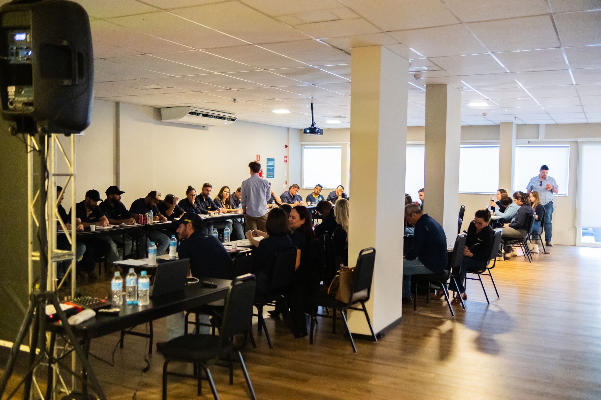 Uma grande sala de conferências com mesas e cadeiras e uma tela de projetor.