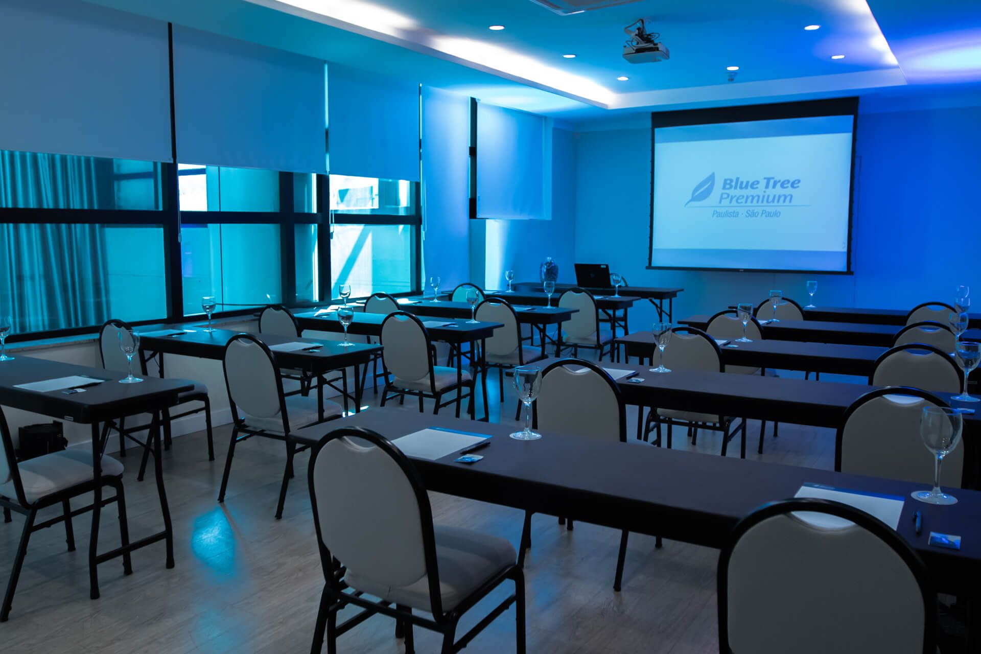 Uma sala de conferências com mesas e cadeiras e uma tela de projetor