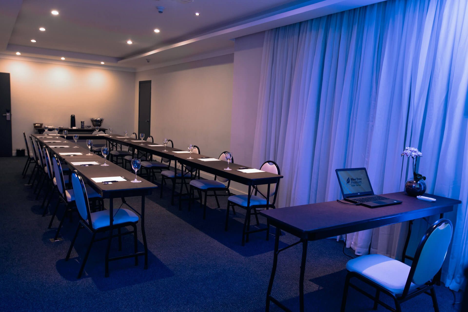 Uma sala de conferências com mesas, cadeiras e um laptop sobre uma mesa.