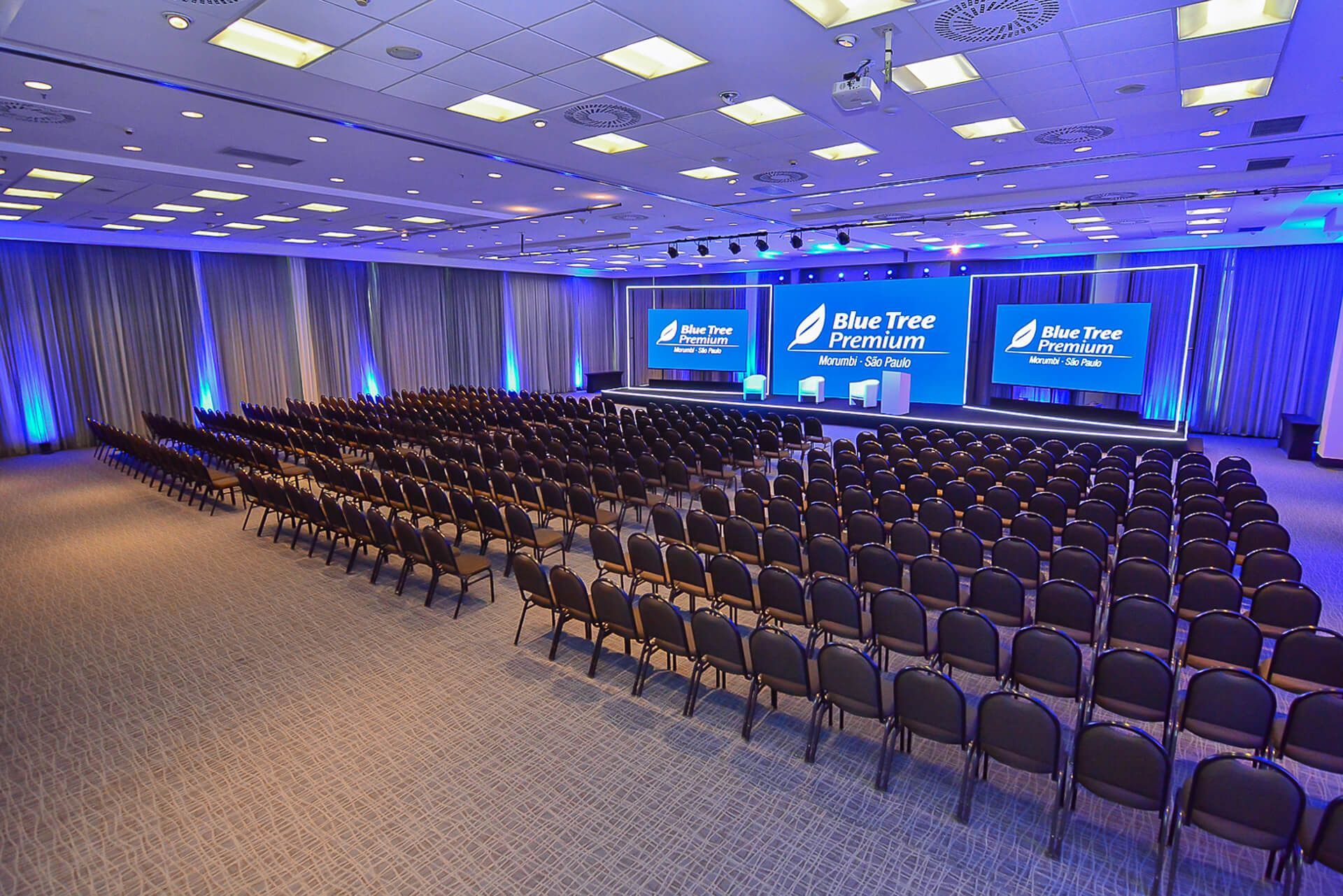 Uma grande sala de conferências com fileiras de cadeiras e um palco.