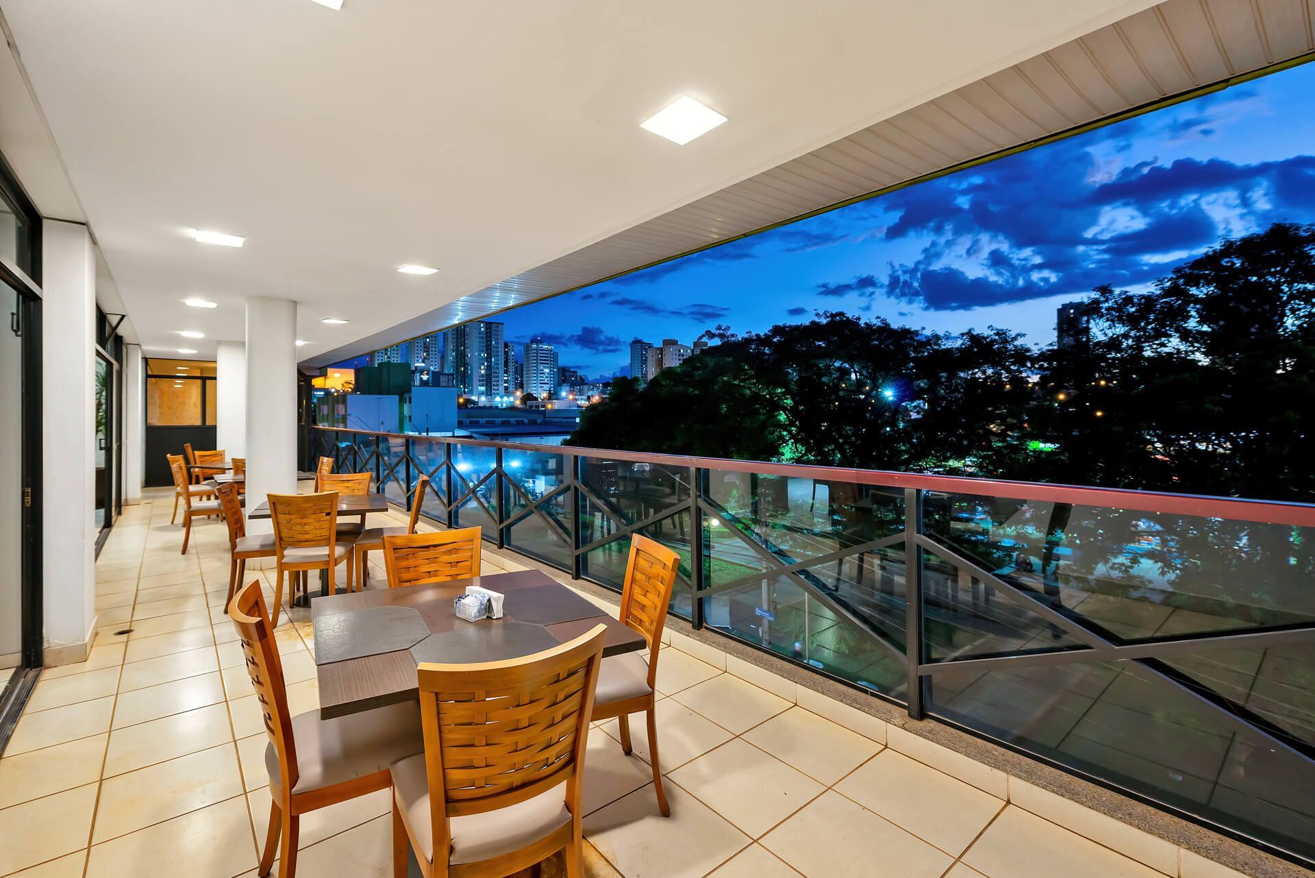 Uma varanda com mesas e cadeiras e vista da cidade à noite.
