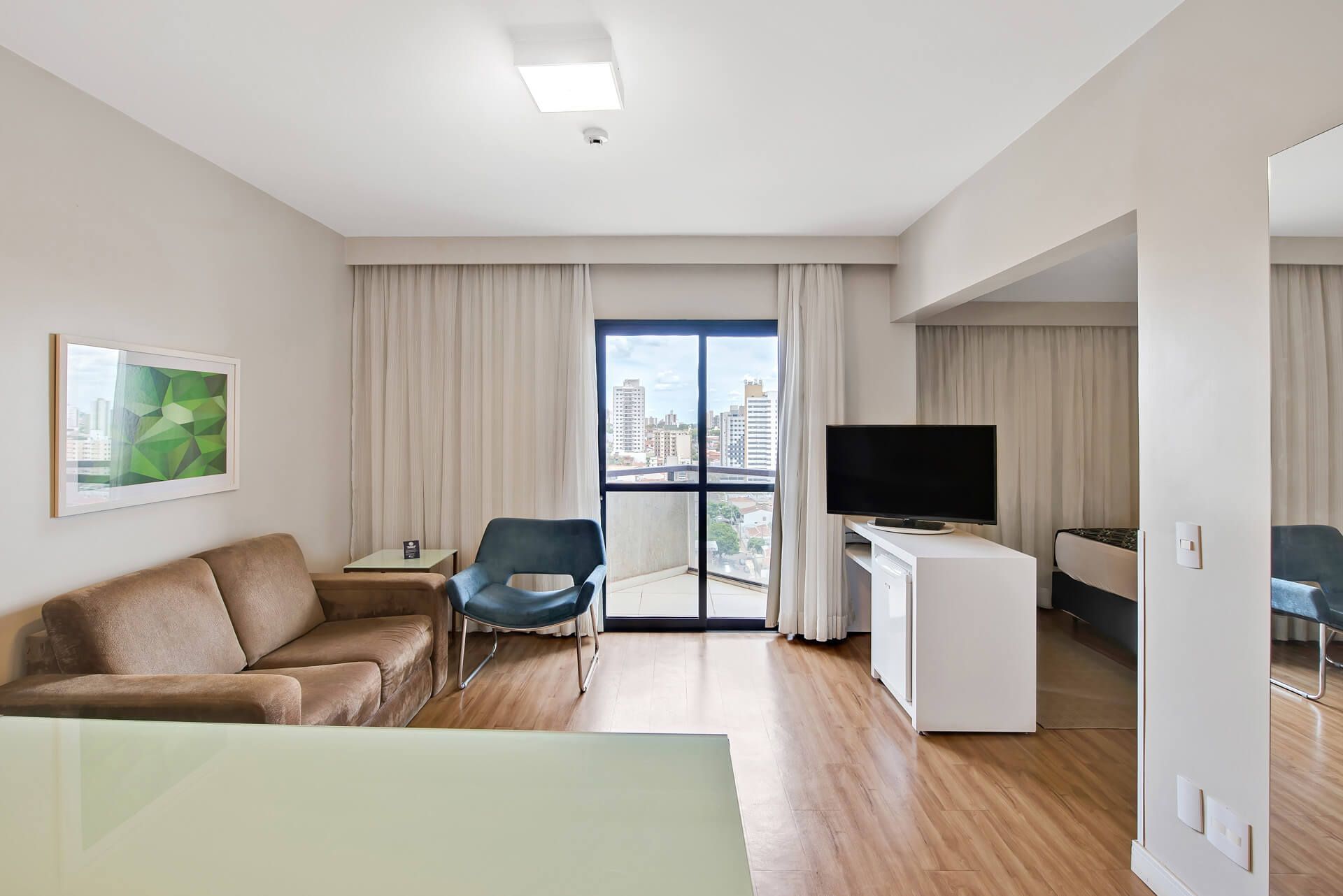 Uma sala de estar com sofá, cadeira, televisão e varanda.