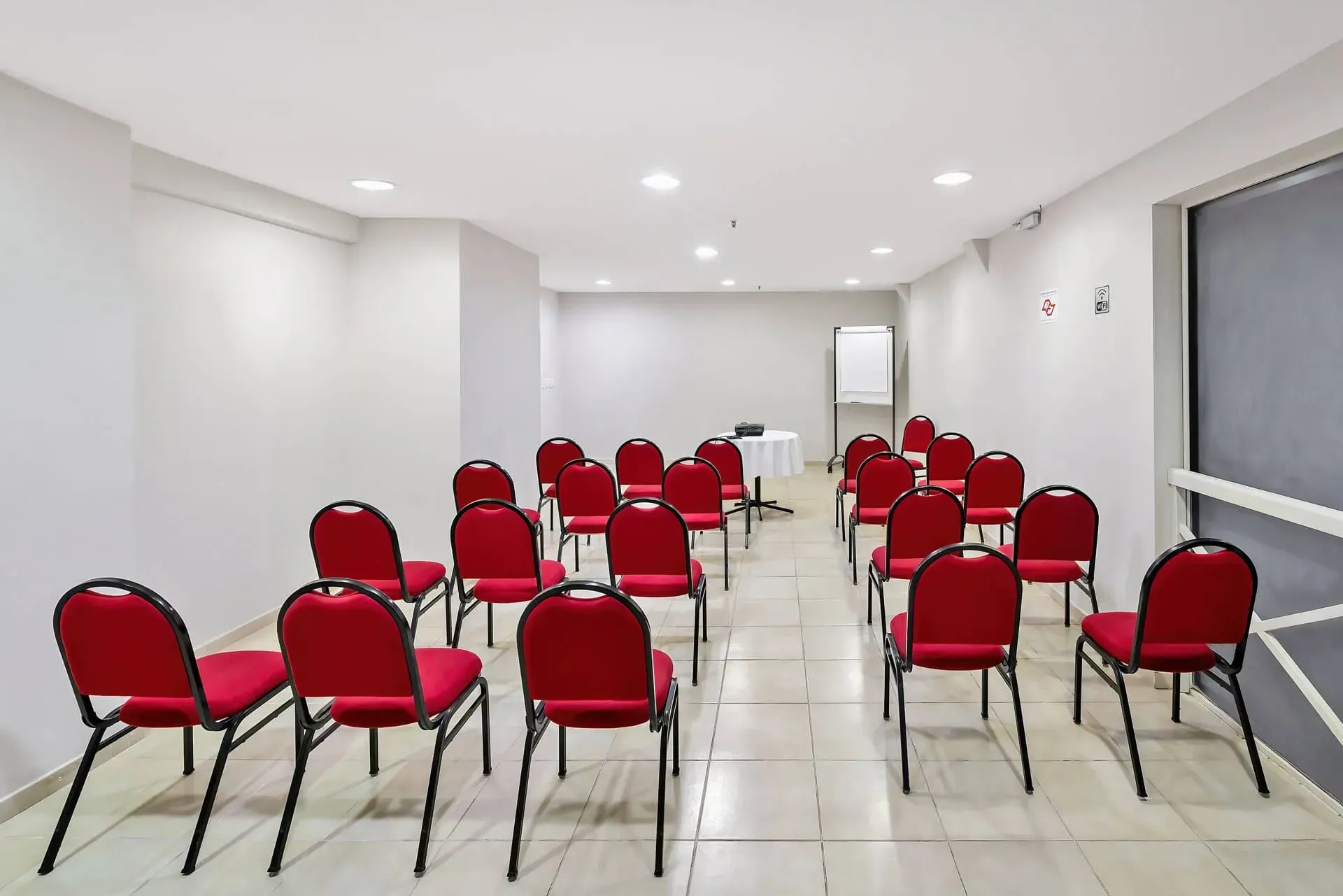 Uma sala grande com mesas e cadeiras e uma tela de projetor.