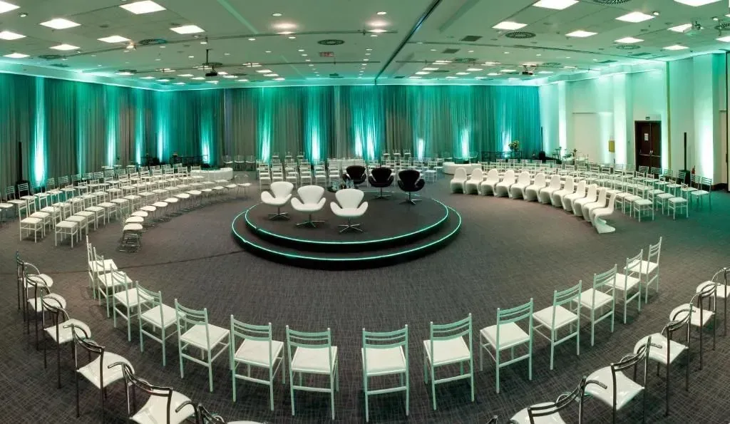 Uma sala grande com mesas e cadeiras e uma tela de projetor.
