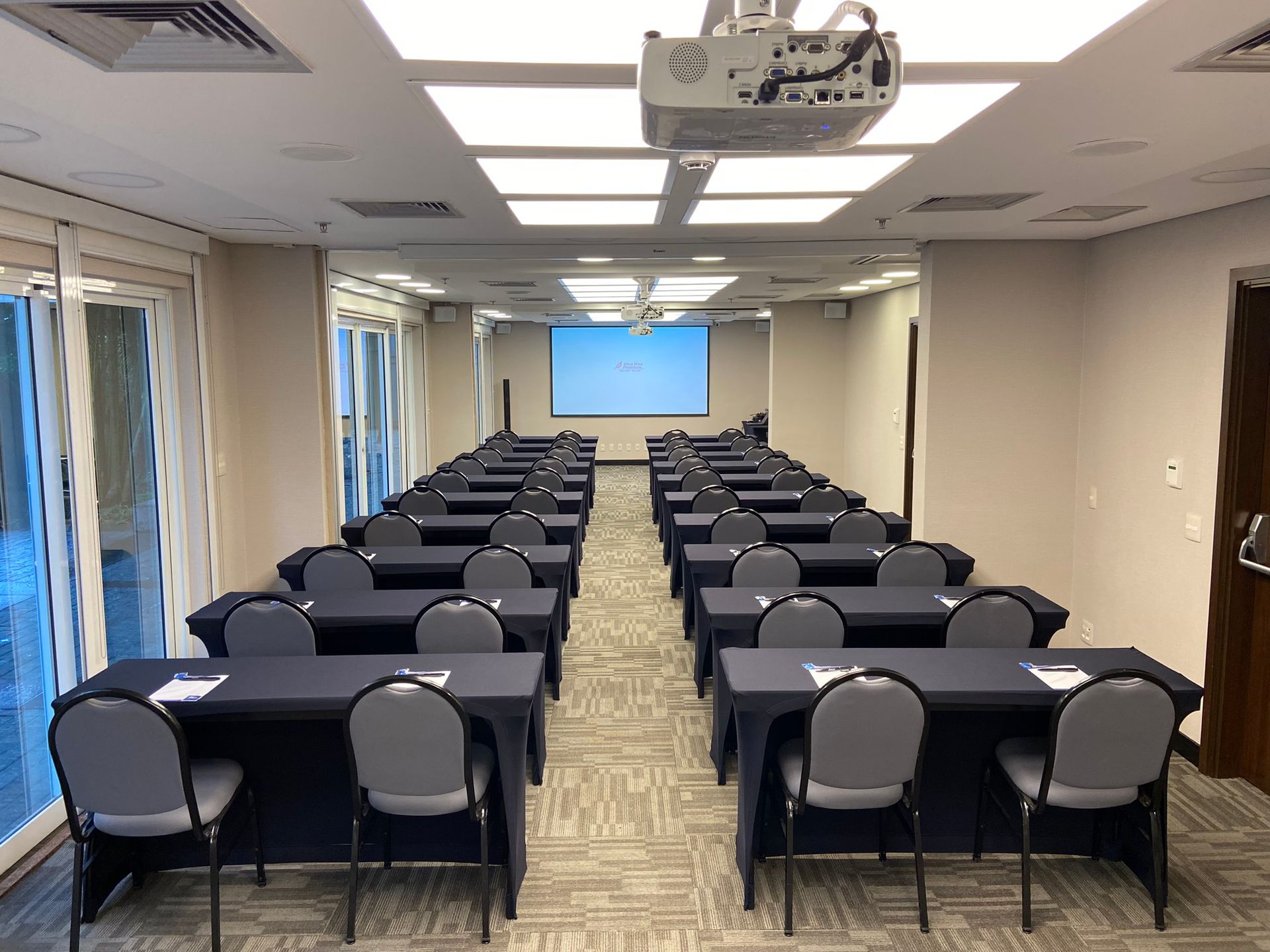 Uma grande sala de conferências com mesas, cadeiras e um projetor.