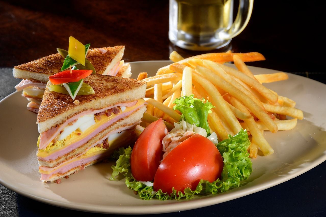 Um sanduíche e batatas fritas em um prato com um copo de cerveja ao fundo.