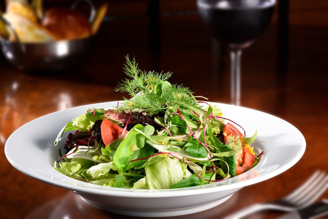 Uma salada em uma tigela branca sobre uma mesa ao lado de uma taça de vinho