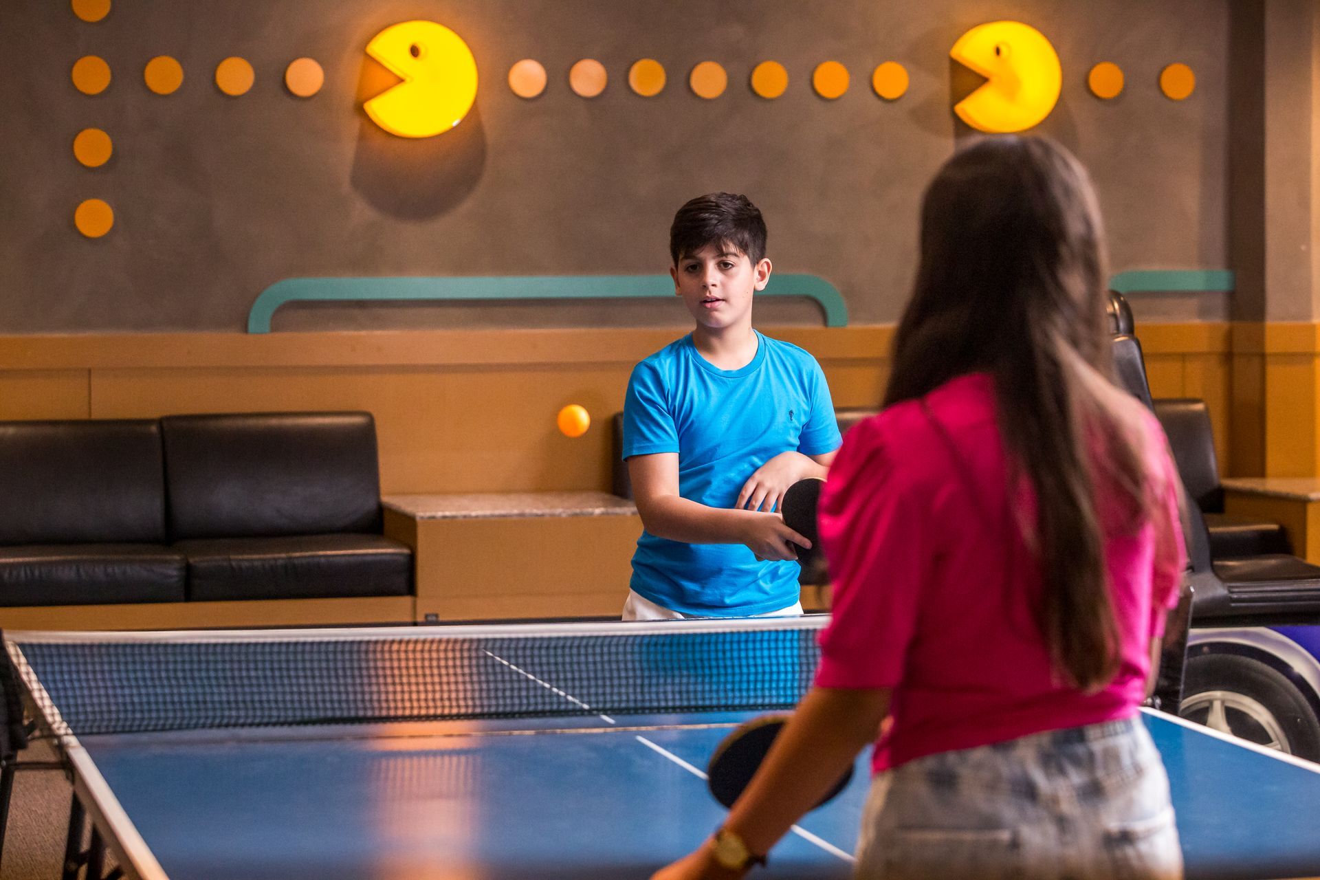 Um menino e uma menina estão jogando pingue-pongue em uma mesa.