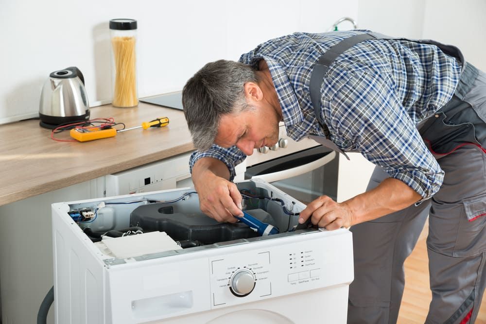 A Man is Fixing a Washing Machine in a Kitchen — Sawtell Electrical Pty Ltd In Coffs Harbour, NSW