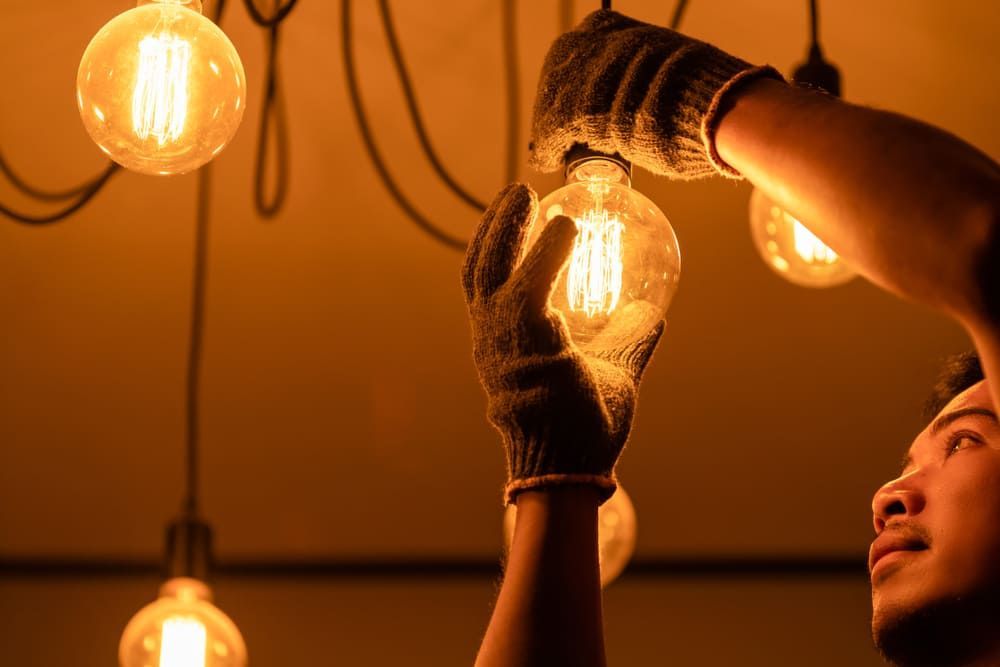A Man is Changing a Light Bulb on a Chandelier — Sawtell Electrical Pty Ltd In Coffs Harbour, NSW