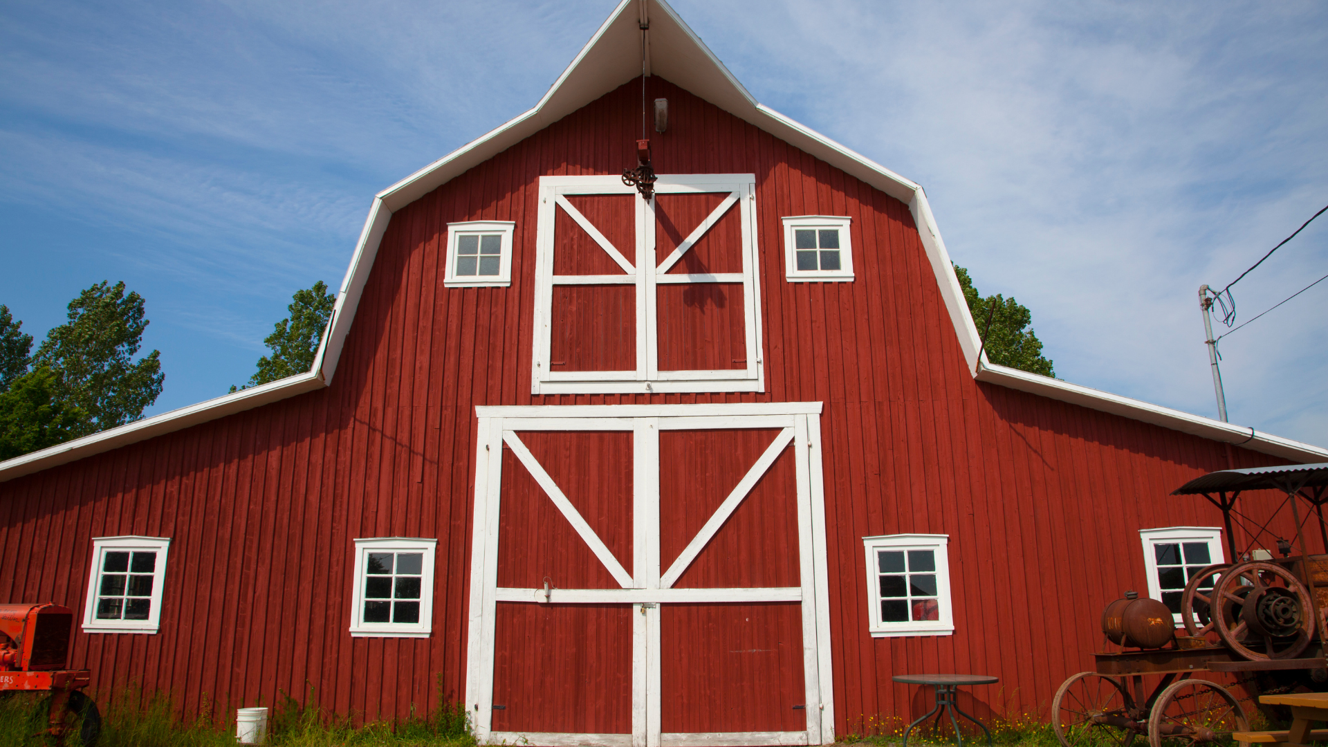 Red barn with white trim and doors, set against a blue sky.