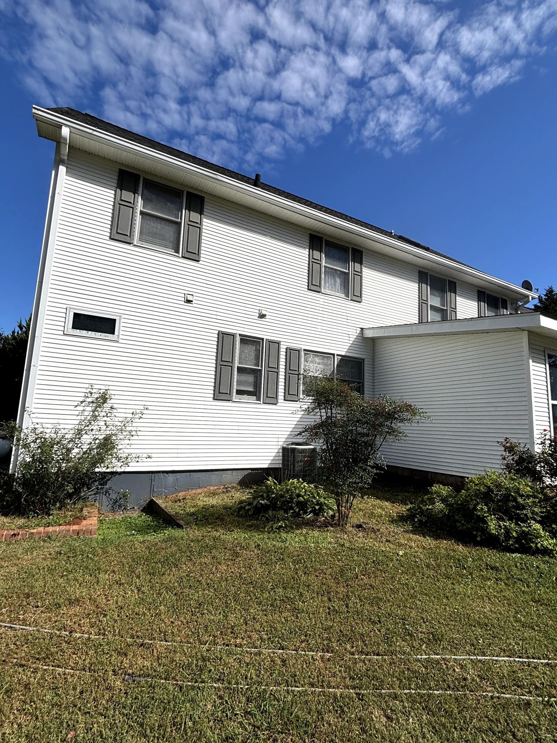 White two-story house with gray shutters and a detached section; blue sky and grass in the foreground.