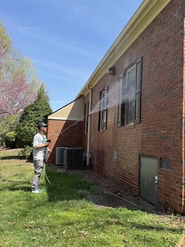 Person power washing a brick building on a sunny day.