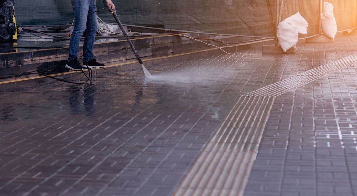 Person power washing a tiled walkway. Water spray is visible, surface is wet.