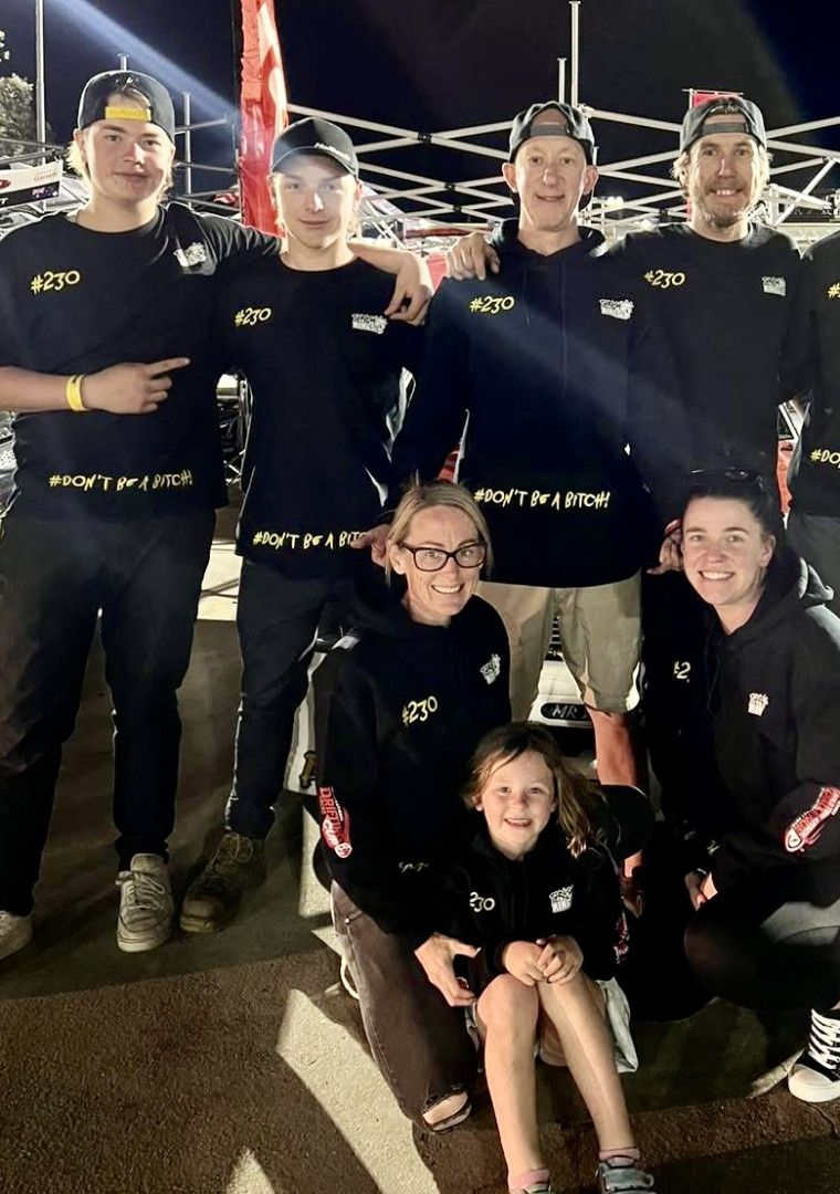 Group of people in black shirts, smiling, pose together outdoors at night, under lights.