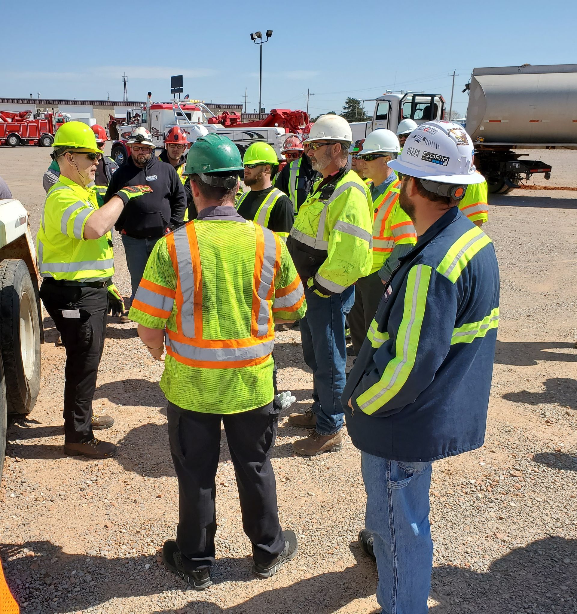 Workers in hard hats and safety vests meeting on a gravel construction site under bright sun