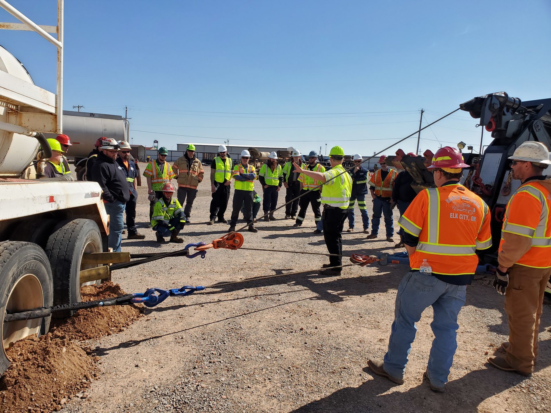 Construction crew gathered around heavy equipment on a gravel site, wearing high-visibility safety gear.