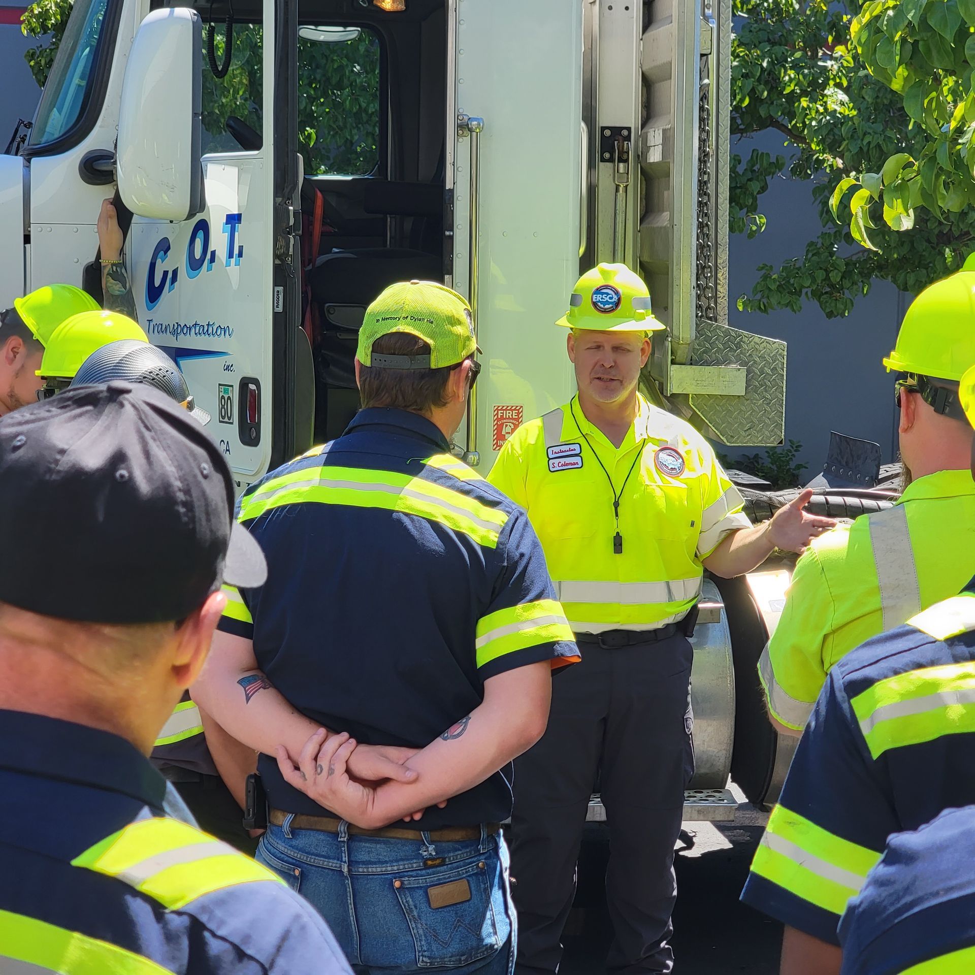 Workers in neon safety gear gather beside a truck during a roadside briefing.