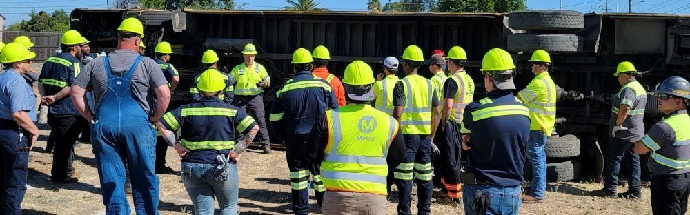 Construction workers in neon hard hats and safety vests gathered at a worksite, seen from behind.