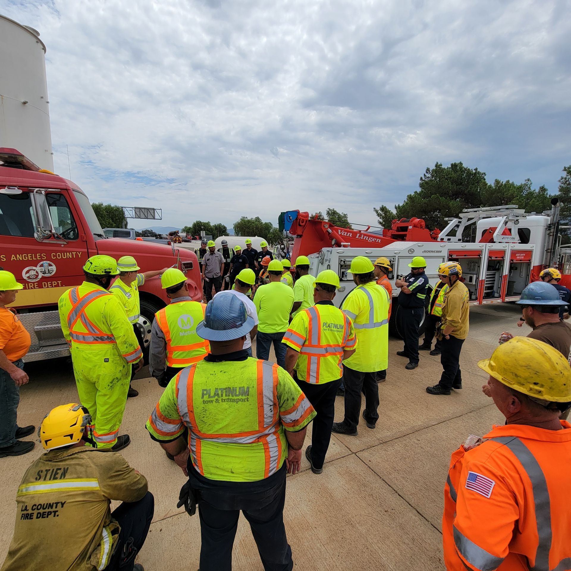Emergency workers in neon safety gear gathered beside fire trucks at a roadside scene.