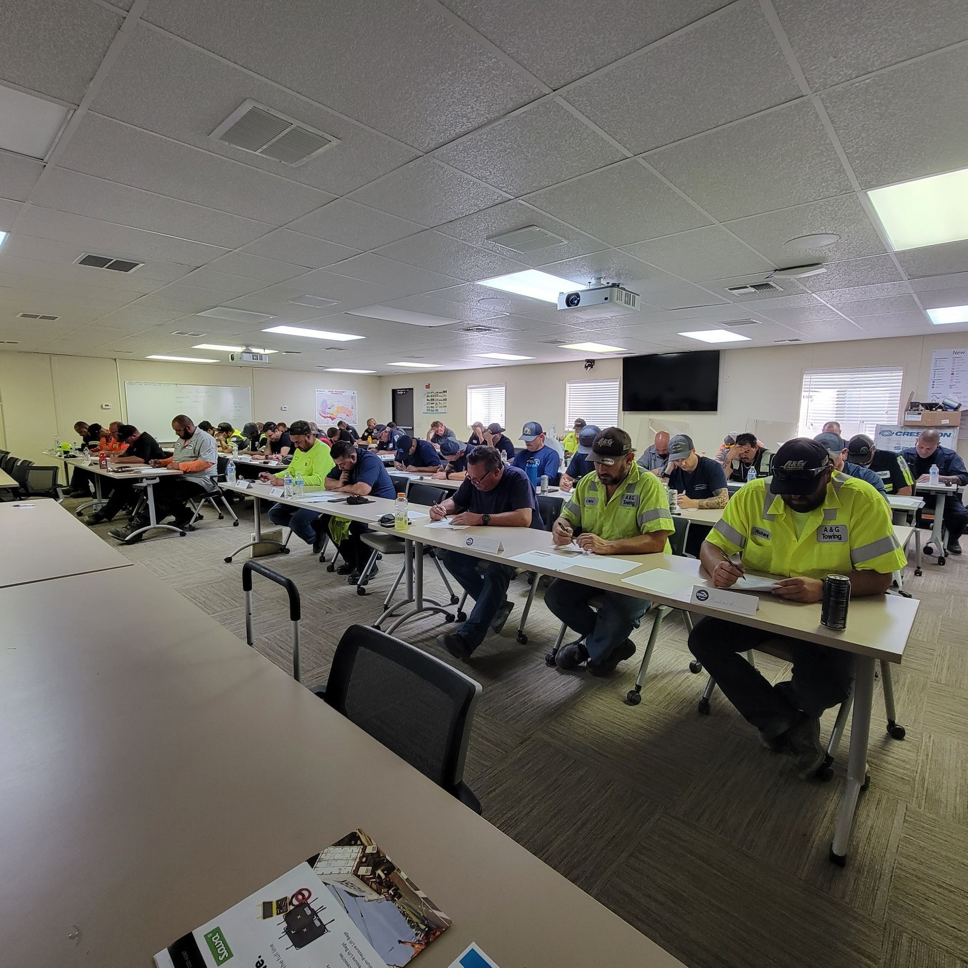 Classroom briefing with workers seated at tables in a bright training room, many wearing hi-vis shirts and masks