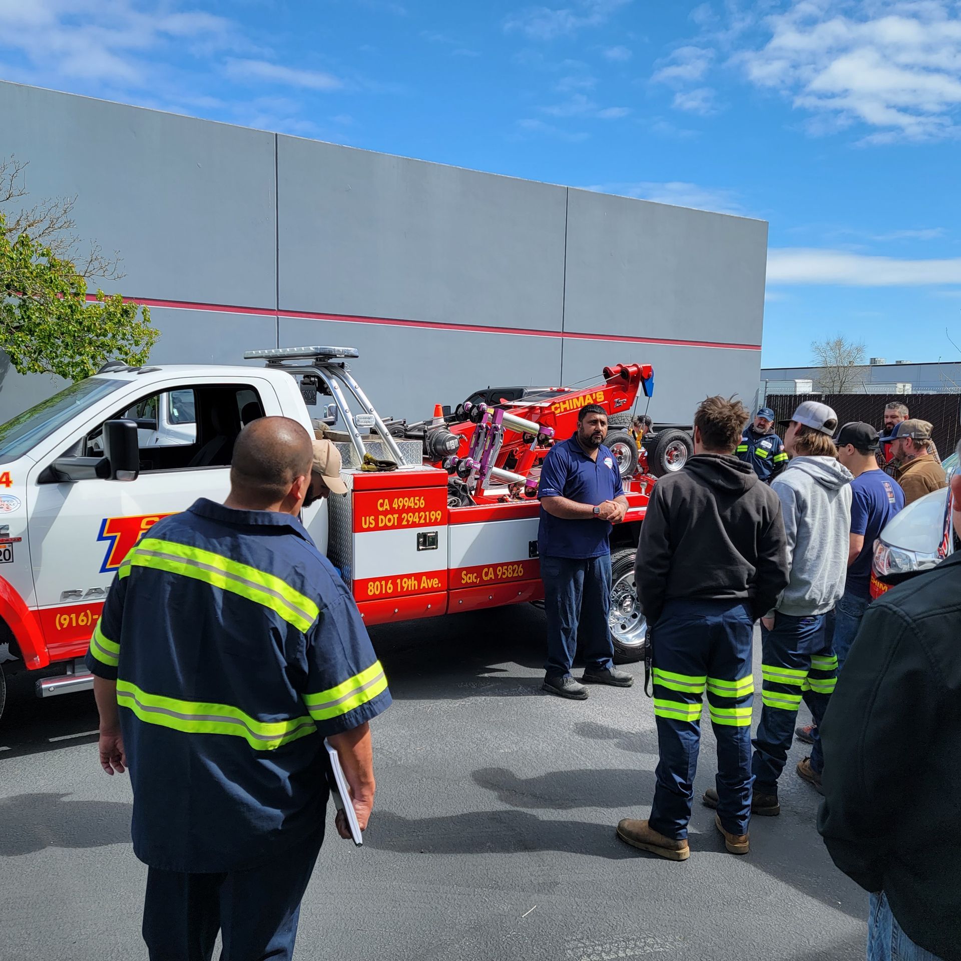 Fire rescue crew gathered around a red tow truck outside a gray building on a sunny day