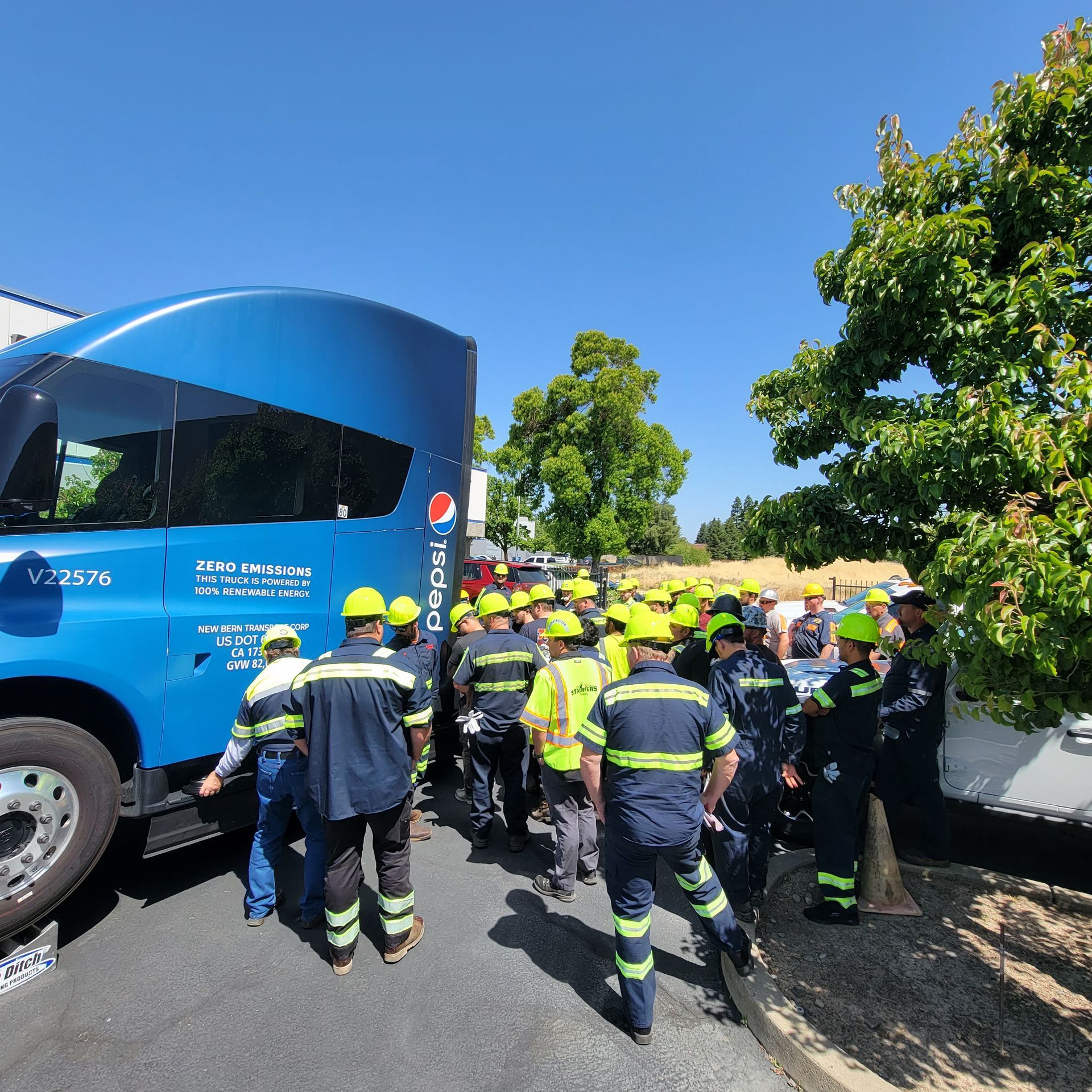Firefighters in yellow helmets gather beside a blue truck on a sunny roadside.