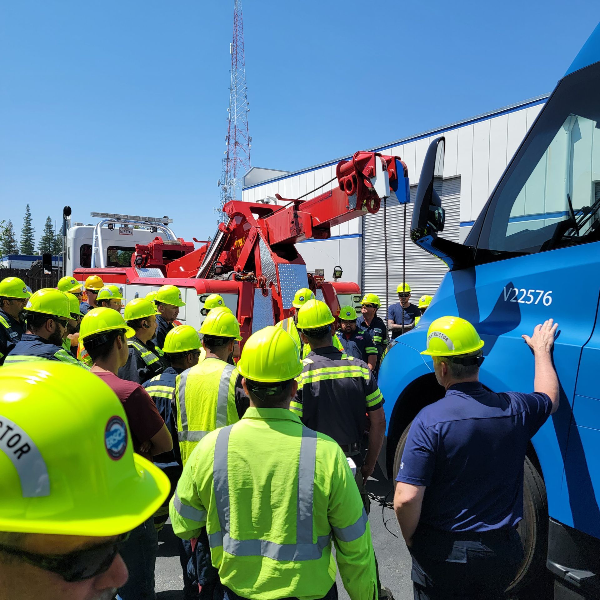 Construction crew in neon safety gear gathered around a blue truck and red crane outdoors.