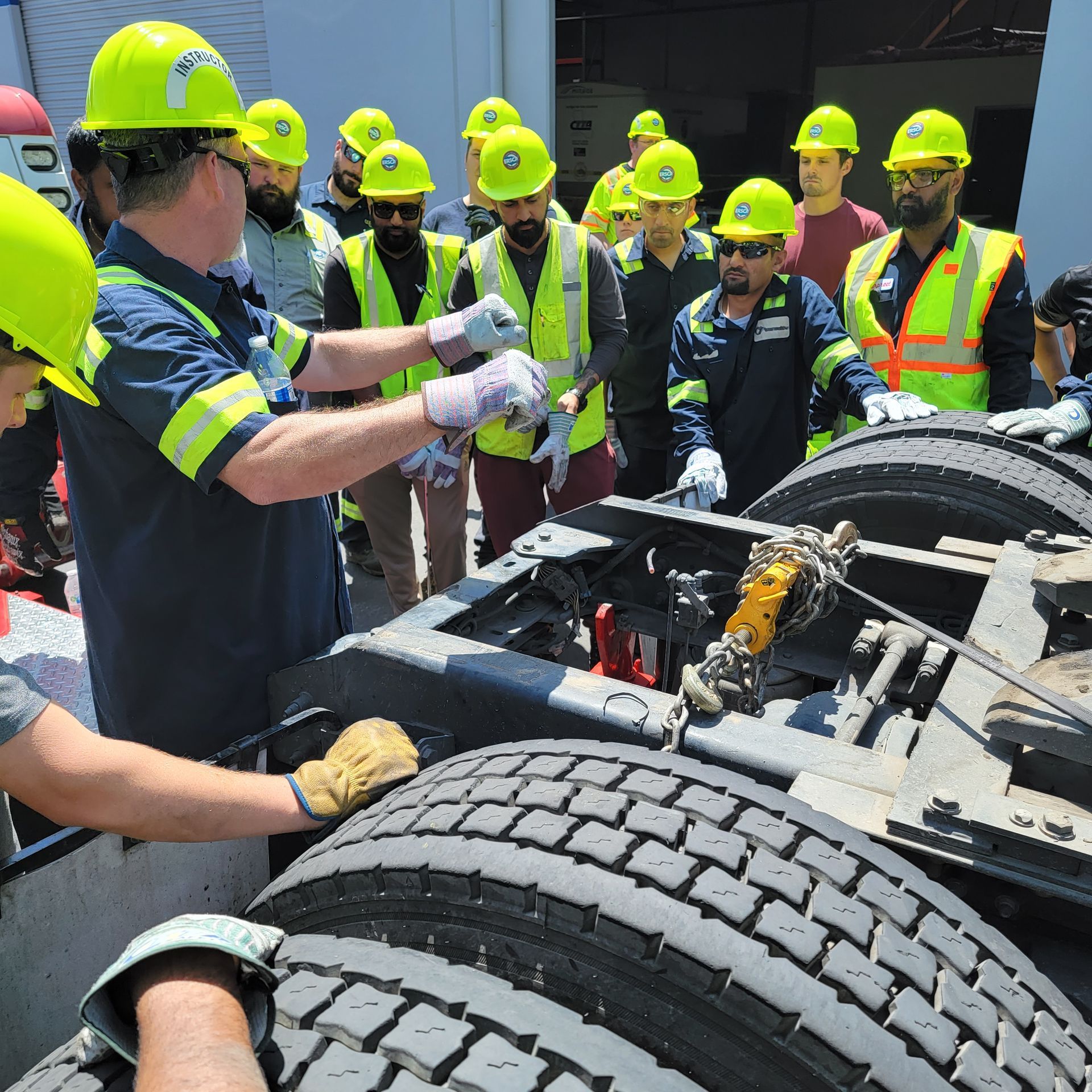 Workers in hard hats inspect a truck chassis and tires at a construction site.