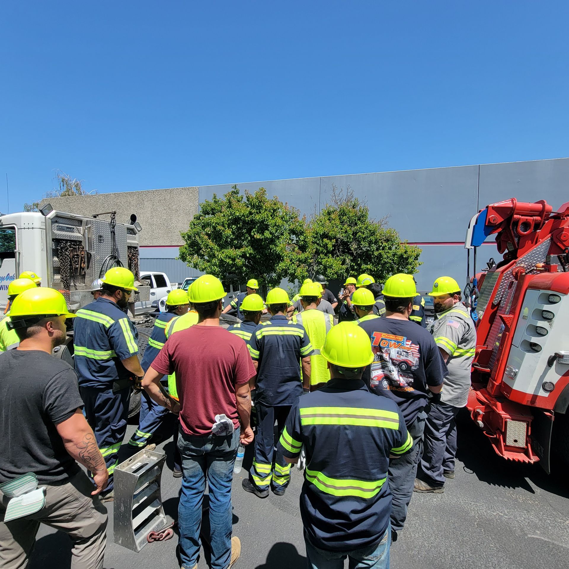 Workers in high-visibility helmets gather beside a red emergency vehicle on a sunny street.