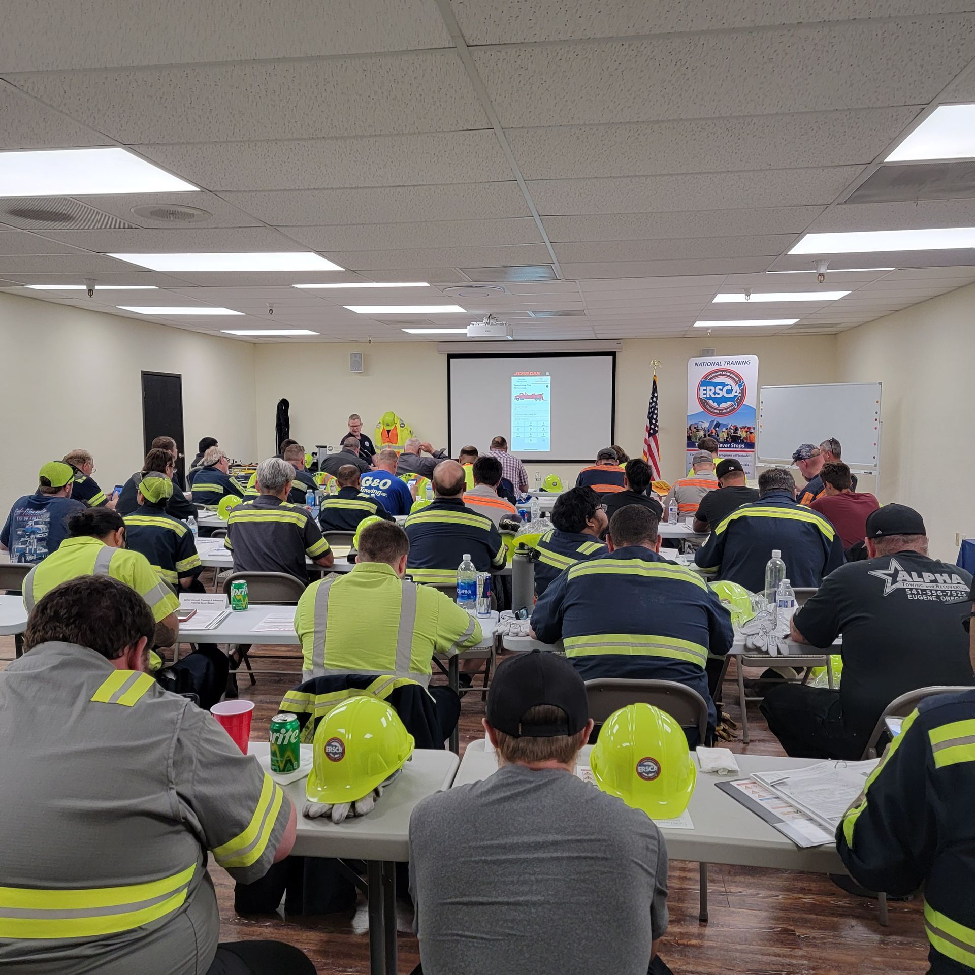 Workers in reflective jackets seated in a training room facing a presentation screen