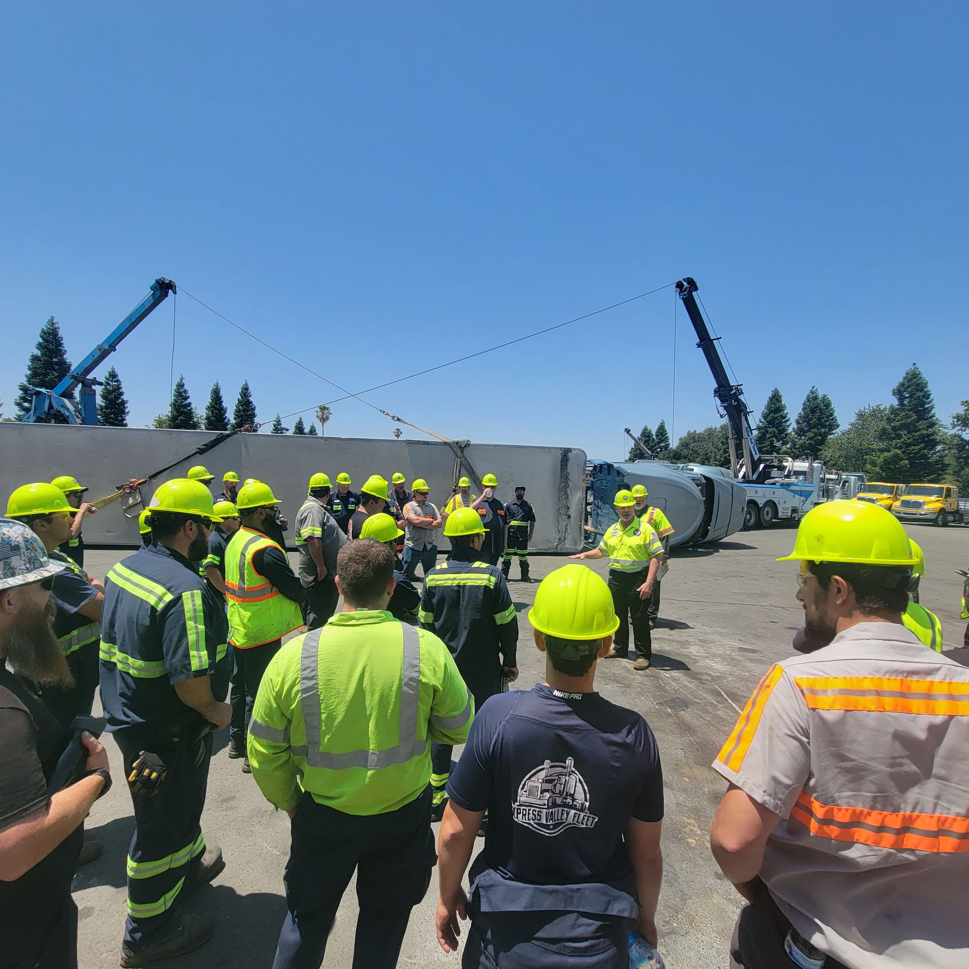 Workers in high-visibility gear gather around a toppled truck at an outdoor accident site