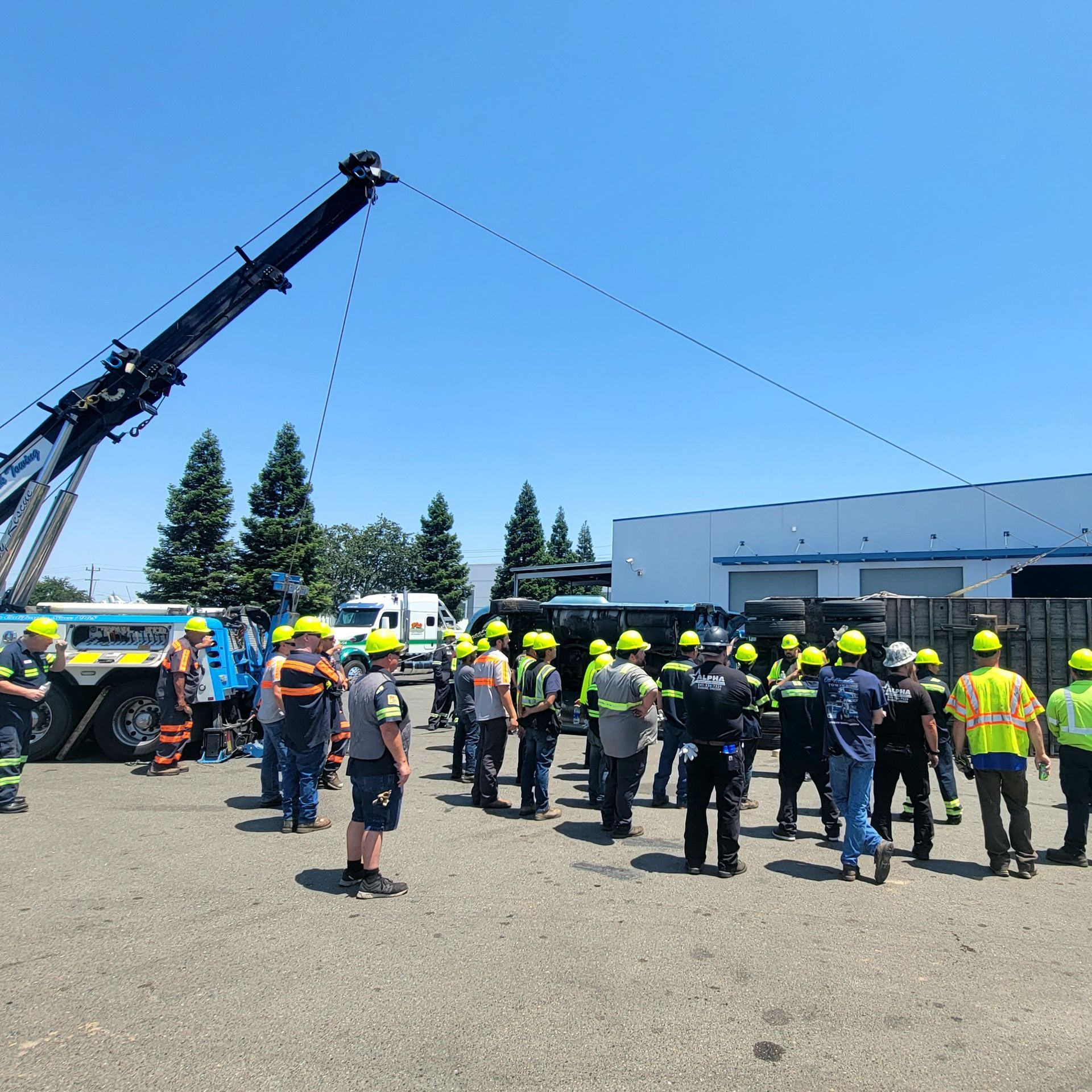 Group of workers in hard hats gathered in a yard beside a raised crane under a clear blue sky