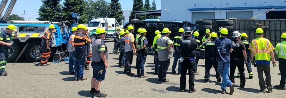 Group of workers in yellow helmets gathered outdoors beside a forklift and trucks at a construction site